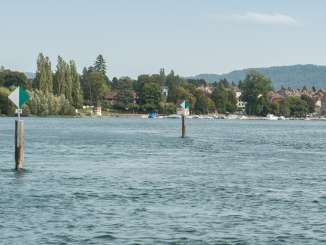 Two whiffs stand in the Rhine. The plaque is divided into a white and a green side and attached to a wooden post. The town of Stein am Rhein can be seen in the background.