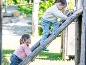 Playground Thayngen Two girls climb up a wooden ladder on a playground.