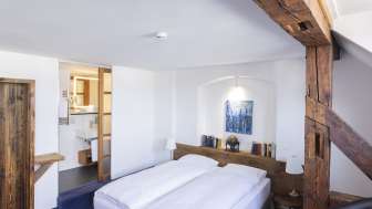 One room has a double bed with white bed linen. The room has wooden elements such as a wardrobe, headboard and beams.