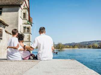 Mother and father sit with their daughter on a stone wall by the Rhine.