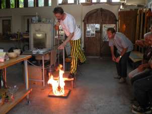A man in yellow and black striped pants demonstrates how to blow glass balls.