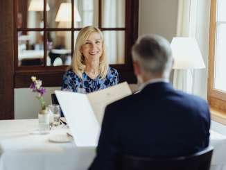 Two people are sitting at a table set with a white tablecloth and looking at the menu.
