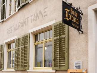 "Restaurant Tanne" is written large on the front of a house. It has green shutters and a black iron sign with gold lettering reading "Hotel Tanne".