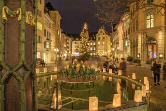 Christmas lights on Fronwagplatz in the old town of Schaffhausen. In the middle is a Christmas tree with a string of lights and there are tea lights on the Mohrenbrunnen fountain