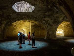 A group with a guide stands in the cash desk of the Munot. Light falls through shafts of light and forms circles on the floor.