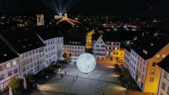 A view from above at night, showing the illuminated Munot. Beams of light shine into the night sky.