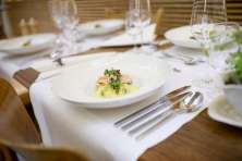 A wooden table is set with white runners. On the table is a white plate with a fish dish.