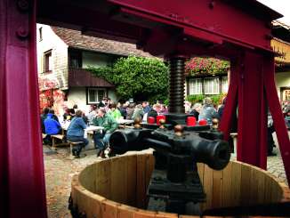 A festival in a courtyard. A large fruit press can be seen in the foreground.