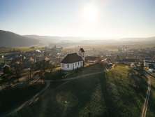 A church stands on a hill with vines. Behind it you can see the village.
