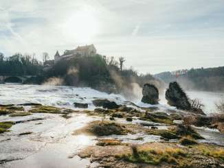 Rhine Falls in winter View of the two Rhine Falls rocks and Schloss Laufen from behind. The air is clear in winter and the sun is reflected in the water.