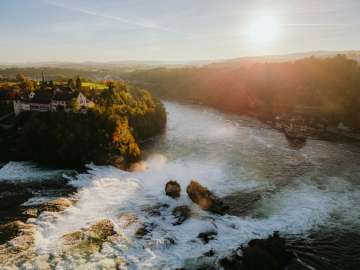 View from above of the two rocks in the waterfall, Schloss Laufen on the left and Schlössli Wörth on the right. Golden evening light shines on the waterfall.
