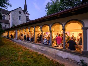 Various stands where you can taste wine are set up in the cloister at Allerheiligen. People are standing at the stalls and drinking wine.