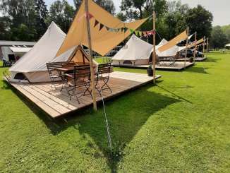 Three glamping tents on a wooden platform. There is a canopy in front of the tent entrance and a table with four chairs.