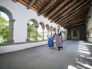 Two women dressed as Huguenots walk through the cloisters of Schaffhausen. One is wearing a blue apron and the other a purple one.