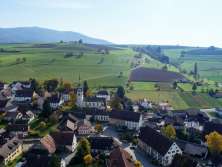 View of the village center of Schleitheim with a church in the middle. Behind the village there are gentle hills with meadows and fields.