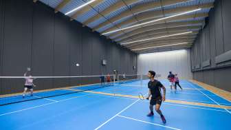 A hall with four blue badminton courts. People are playing badminton on them.