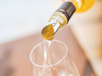 White wine is poured into a wine glass. You can only see the top of the bottle with the drip guard.