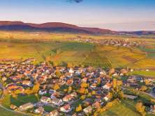 You can see a village from above in the autumnal evening light. The village is surrounded by vines, meadows and fields as well as gentle hills.