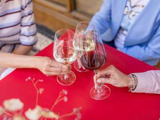 Wii Thursday Three people toast with two glasses of white wine and a glass of red wine. They are sitting at a small red table.