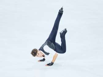 Lukas Britschgi, figure skater, strikes a pose on the ice. He is standing on both hands.