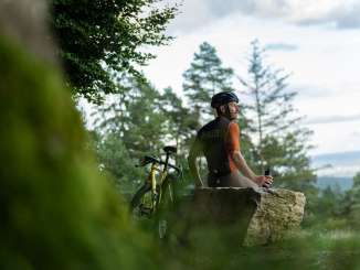 A cyclist is sitting on a large rock, taking a break during his gravel ride.
