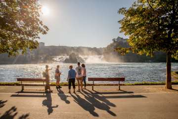 A group with a guide stand in front of the Rhine Falls, the largest waterfall in Europe.