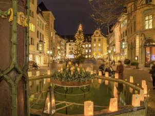 Christmas lights on Fronwagplatz in the old town of Schaffhausen. In the middle is a Christmas tree with a string of lights and there are tea lights on the Mohrenbrunnen fountain