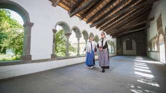 Two women dressed as Huguenots walk through the cloister of Schaffhausen. One wears a blue apron and the other a purple apron.
