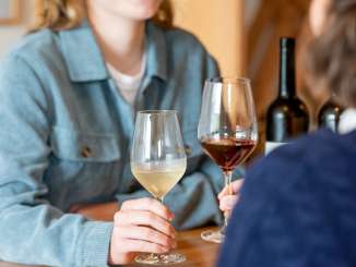 Two friends are sitting at a wooden table. One woman is holding a glass of white wine and the other a glass of red wine.