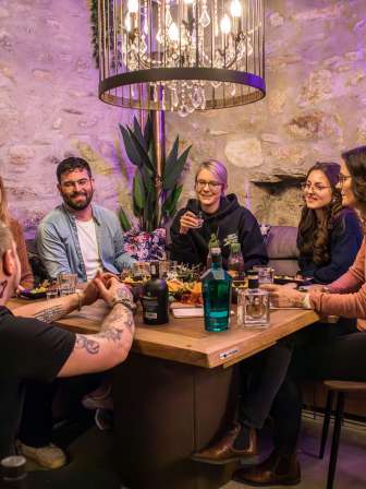 A group is sitting at a wooden table. On it is an aperitif platter and various bottles of gin for tasting.