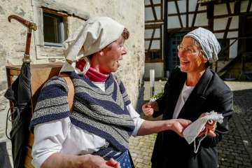 Two women dressed as market traders chat with each other.