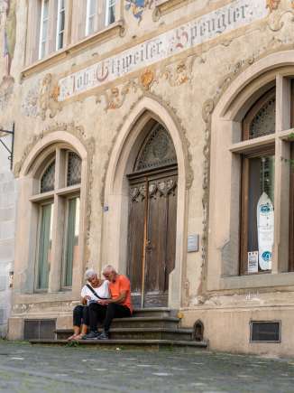 Zwei Touristen sitzen auf einer Treppe vor einem Haus mit Fassadenmalereien und studieren den Stadtplan Stein am Rhein.