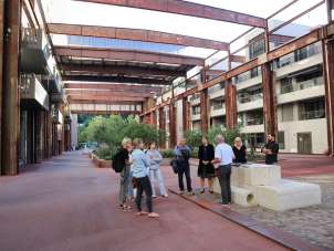 A group with a guide stands in the steel foundry. Large steel girders cross the inner courtyard between the houses.