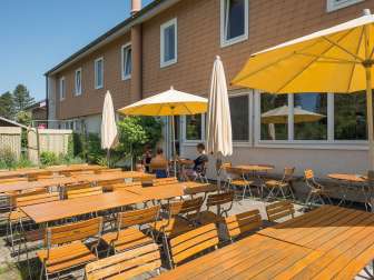 A terrace with wooden tables and chairs and parasols. A group sits around a table.