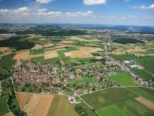 You can see an aerial view of a village surrounded by fields and meadows.