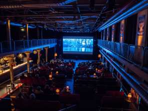 Schaffhausen Film Festival An event hall has been converted into a movie theater. There are various chairs and fabric armchairs and a large screen hangs at the very front.