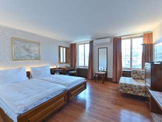 Double room Hotel Rheinfels. A double bed with white bed linen stands on a dark wooden floor. The walls are covered with flowery wallpaper.