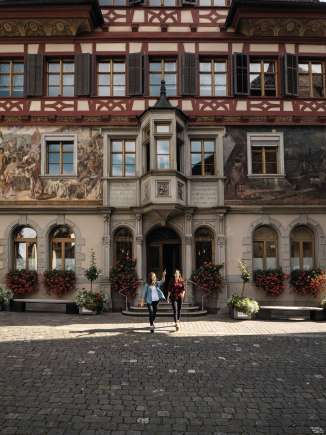 Two friends stand in front of the town hall in Stein am Rhein and look at the facade paintings.