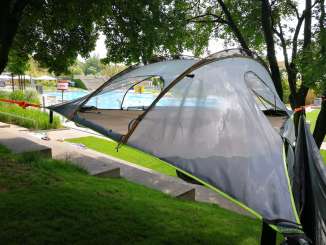 A tree tent stretched between 3 trees. In the background is the outdoor swimming pool.