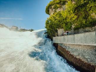 Personen stehen auf einer Aussichtsplattform direkt am Rheinfall.