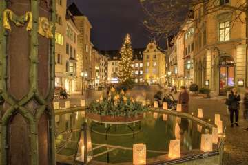 Christmas lights on Fronwagplatz in the old town of Schaffhausen. In the middle is a Christmas tree with a string of lights and there are tea lights on the Mohrenbrunnen fountain