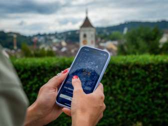 Foxtrail GO Schaffhausen One hand holds a cell phone. On it you can see the digital puzzle Foxtrail GO.