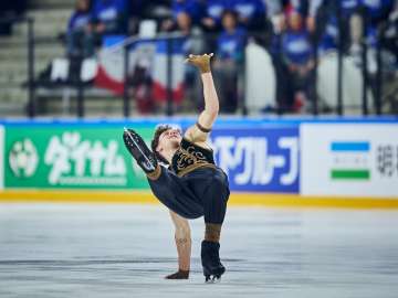 Lukas Britschgi during his figure skating program. He is wearing black pants and a black sleeveless top with gold embellishments.