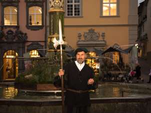 Landsknecht stands in front of the Landsknecht fountain on Fronwagplatz in Schaffhausen. It is already dark.