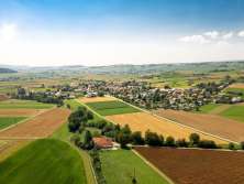 Village from above surrounded by meadows and fields with far-reaching views over a slightly hilly landscape with several villages.