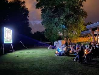 People are sitting on a lawn in front of a screen, watching short films.