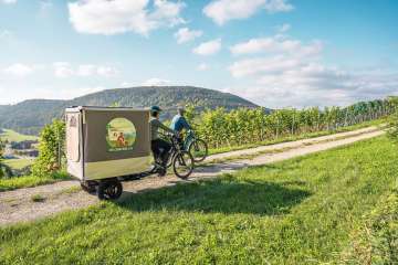 Two friends are out and about in the vineyards on their e-bikes. A Cargovelo has a fold-out tent structure.