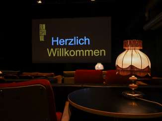 Schaffhausen Film Festival In a dark room, various red sofas and armchairs serve as movie theater chairs. The big screen reads "Welcome".