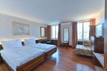 Double room Hotel Rheinfels. A double bed with white bed linen stands on a dark wooden floor. The walls are covered with flowery wallpaper.