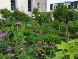 A garden with blooming flowers in purple and pink. An old house stands in the background.